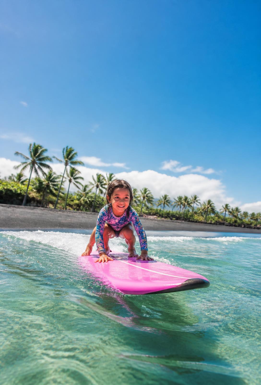A young surfer riding a wave off Guatemala's black-sand Pacific coast under a bright blue sky